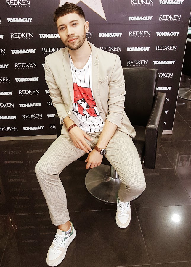A man with a revolutionary hairstyle, which is fading in the sides, with fringe, complemented by suit in the shades of pearl & a white shirt with the Snoopy cartoon. Plus wearing a ecological sneakers in the same tones.  